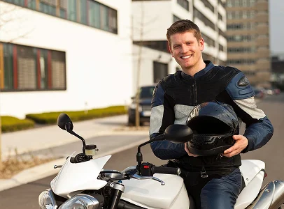 Homme souriant en tenue de moto, assis sur une moto blanche et tenant son casque à Villeneuve‑sur‑Lot et à Saint‑Sylvestre‑sur‑Lot dans le Lot‑et‑Garonne 47