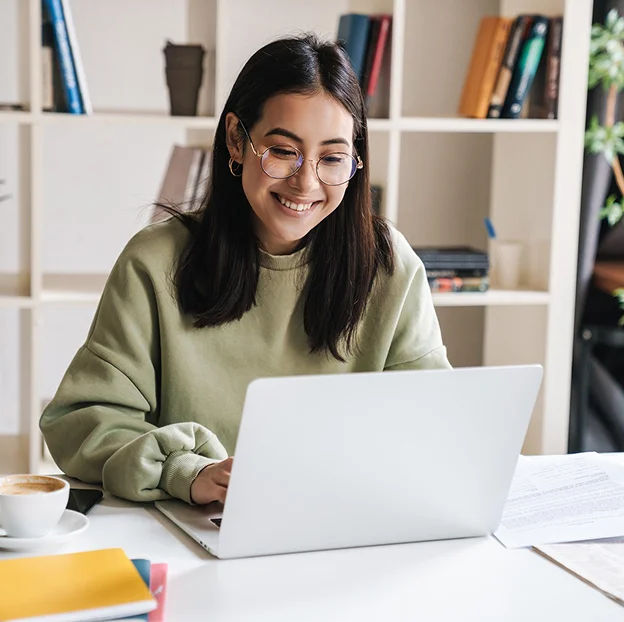 Jeune femme souriante avec des lunettes, travaillant sur un ordinateur portable.